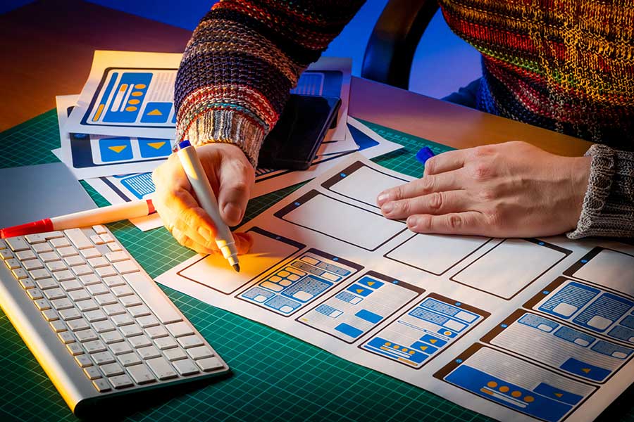 Close-up of e-learning course designer’s hands holding a felt marker, with Apple keyboard and paper storyboards on desk