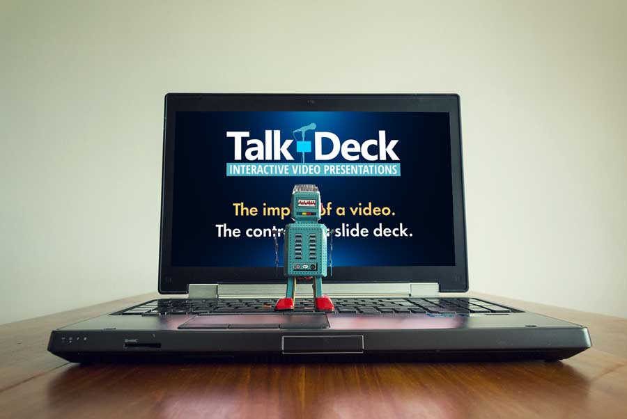 Stylized robot in front of a laptop displaying a Talk-Deck title slide, symbolizing the intersection of AI and presentations.